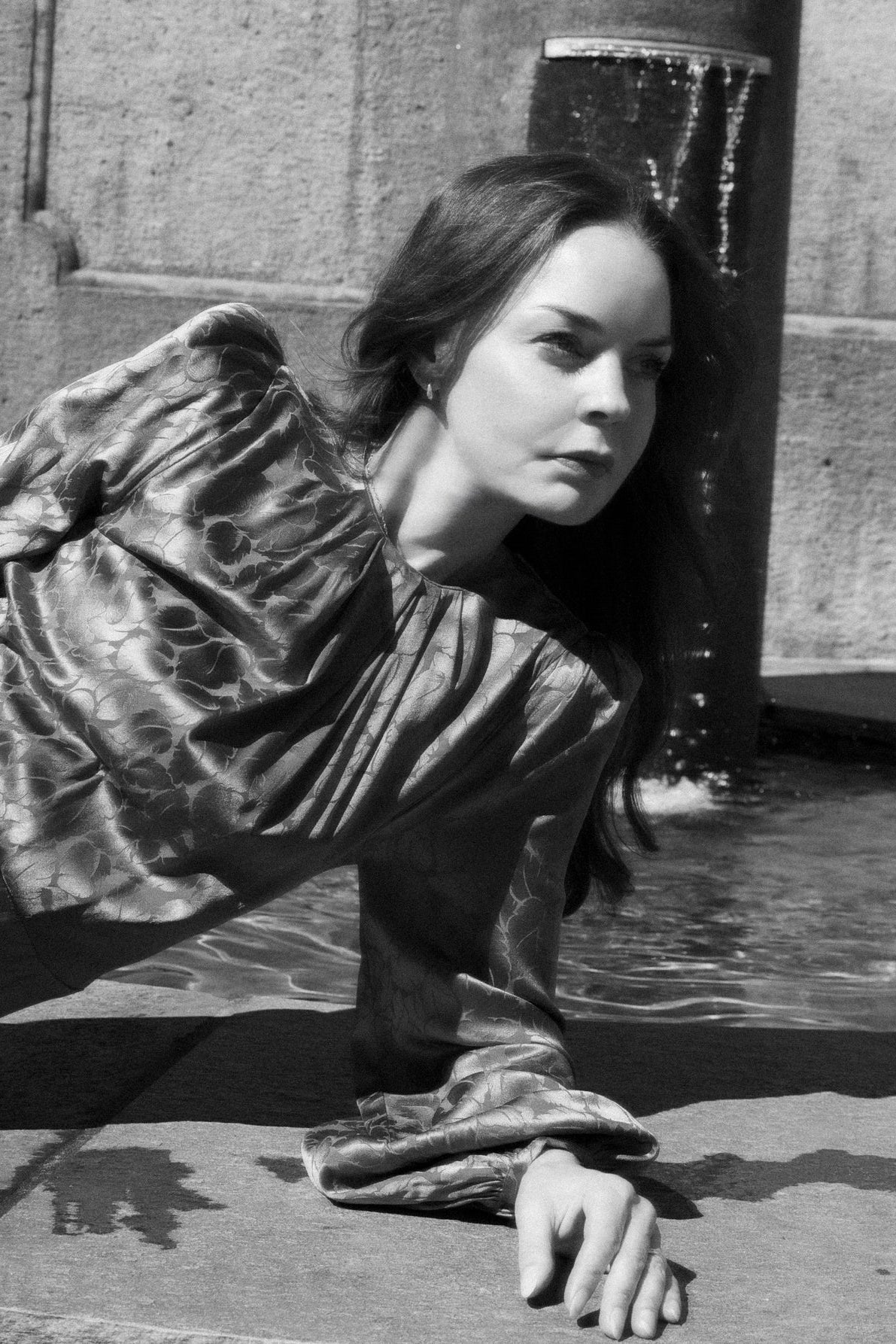 Woman in a flowing dress lying on a stone surface with a building in the background
