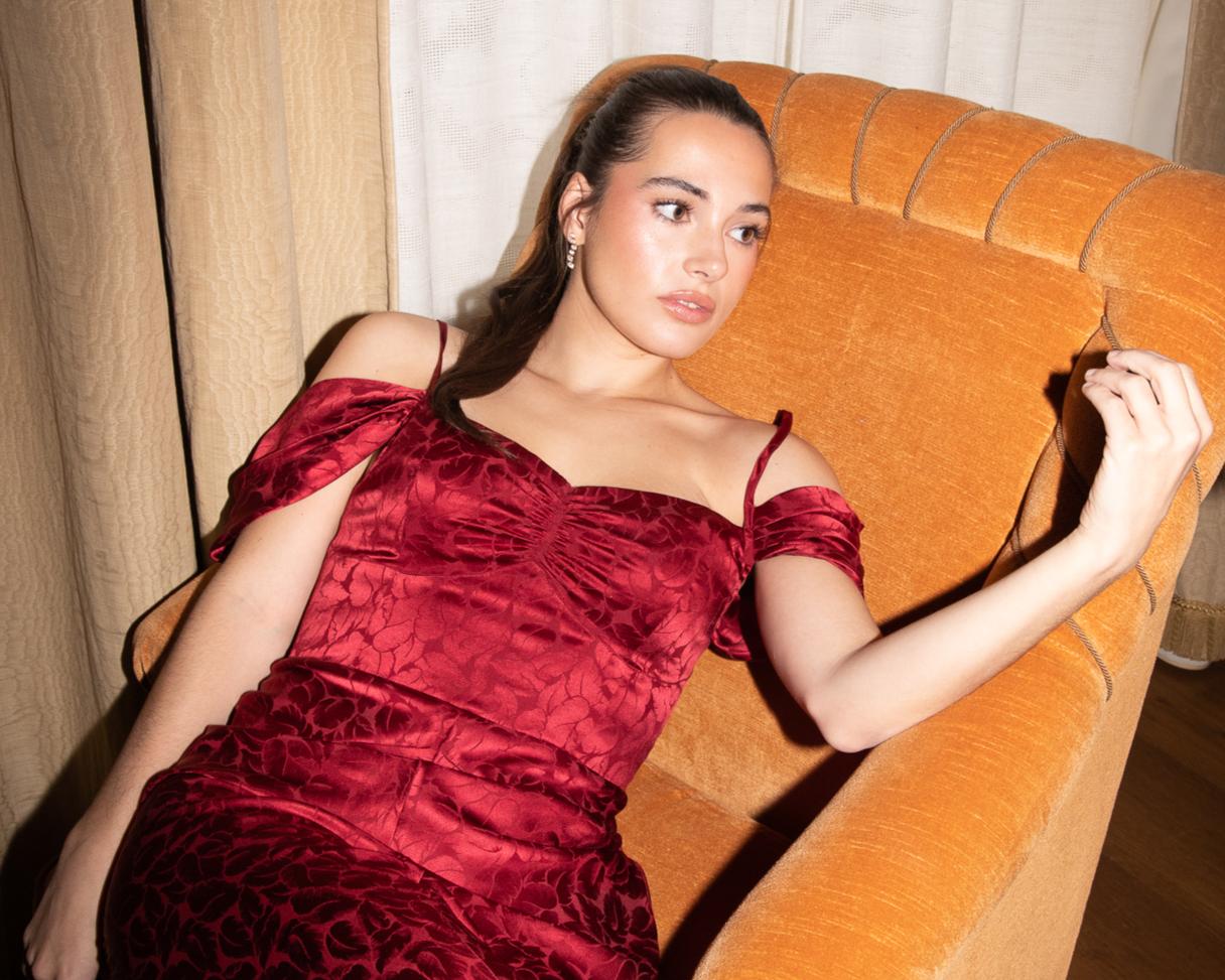 Woman in a red dress sitting on an orange couch with curtains in the background