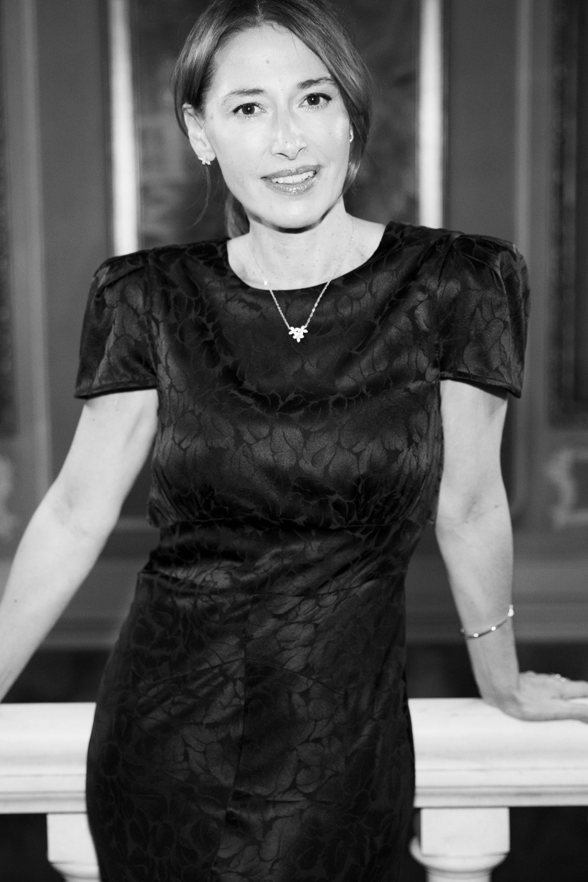 A black short-sleeve textured dress with a crew neck, worn by a woman posing in front of a white balustrade.