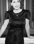 A black short-sleeve textured dress with a crew neck, worn by a woman posing in front of a white balustrade.